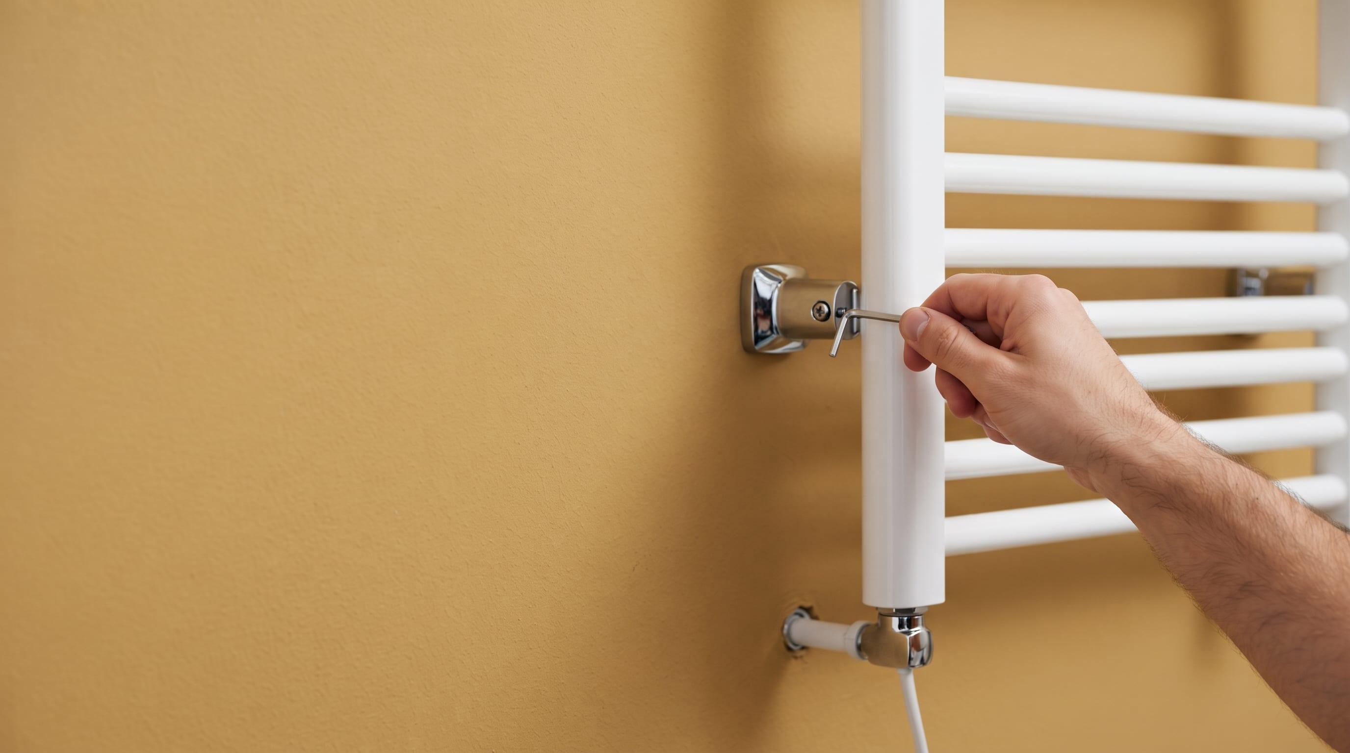 Fixation murale d'un sèche-serviette électrique blanc dans une salle de bain, réglage de la patte de fixation à la clé